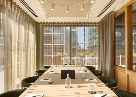 A contemporary meeting room featuring a conference table, upholstered chairs, floor-to-ceiling windows, sheer curtains and views of an outdoor terrace.