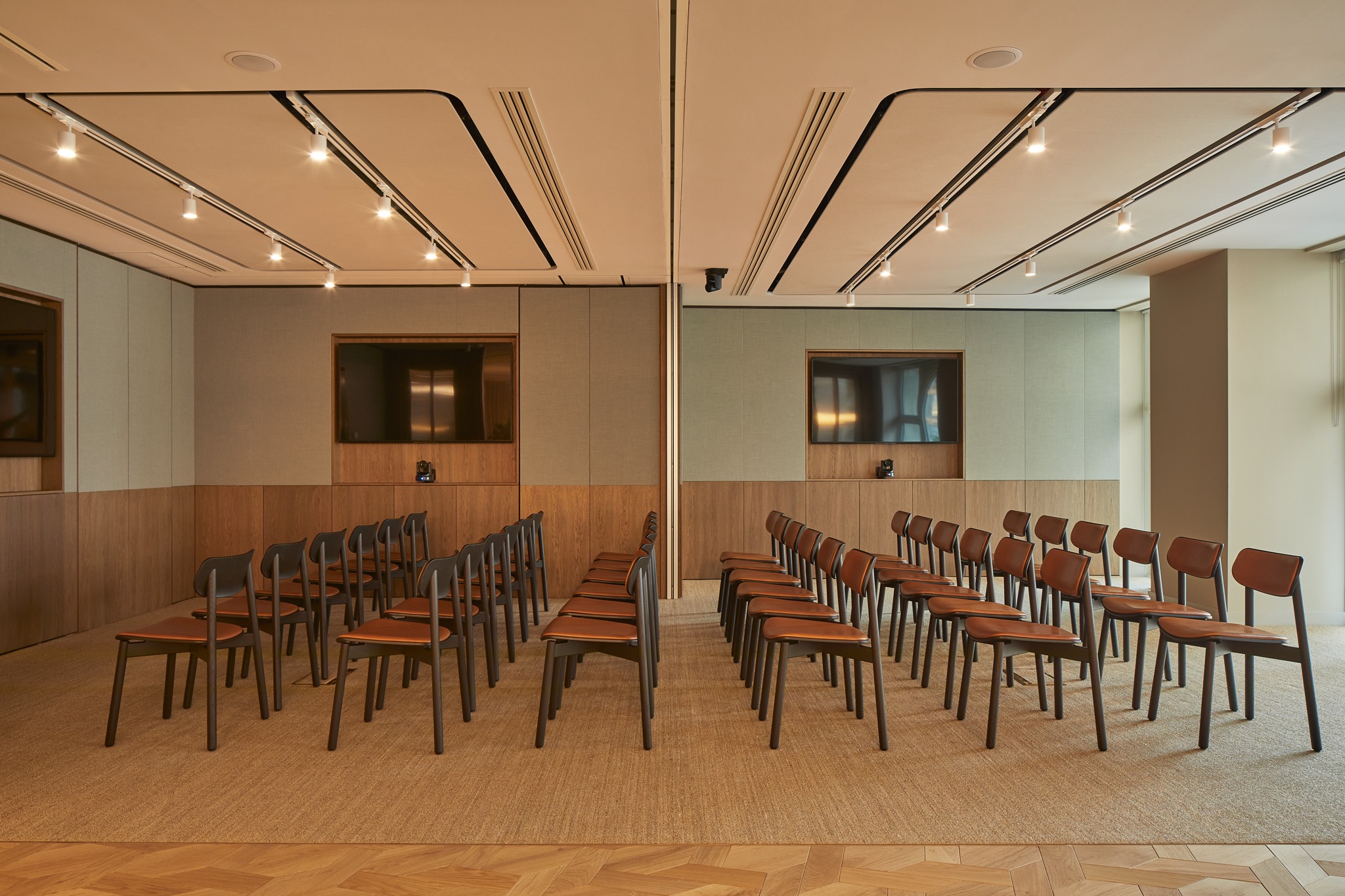A contemporary event space arranged in a theatre-style layout with rows of chairs, presentation screens and a movable partition dividing the room into two sections.