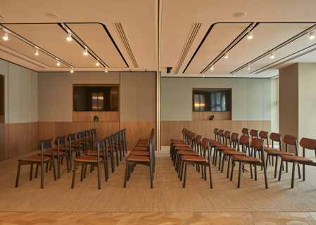 A contemporary event space arranged in a theatre-style layout with rows of chairs, presentation screens and a movable partition dividing the room into two sections.