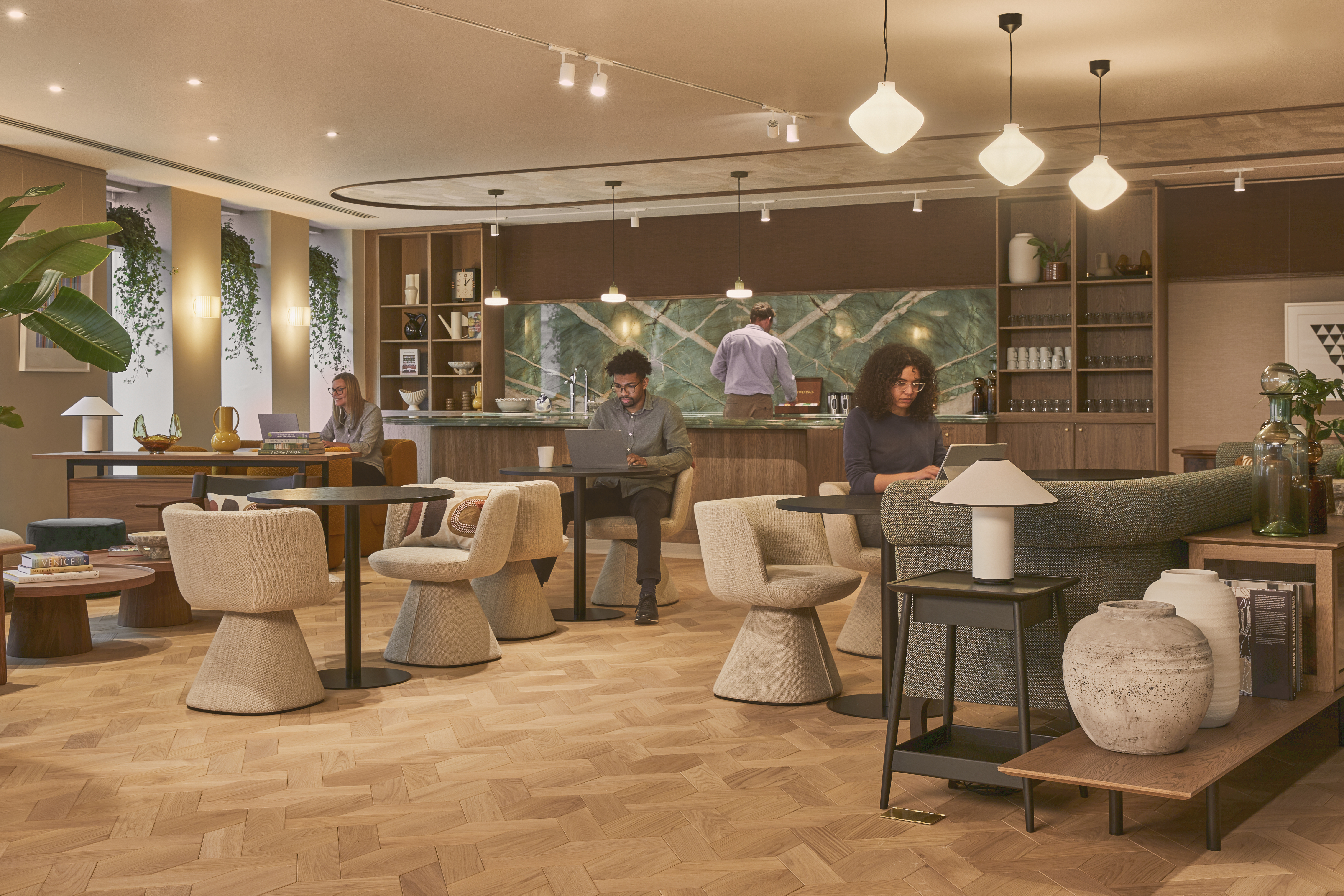A modern breakout lounge with comfortable seating, café-style tables, a communal kitchen and people working in a contemporary office environment.