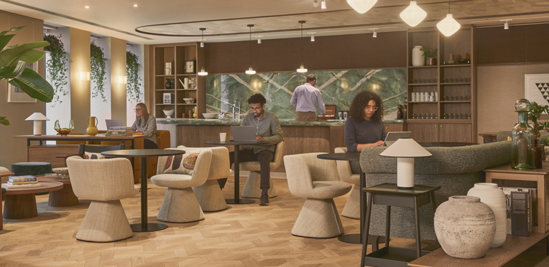 A modern breakout lounge with comfortable seating, café-style tables, a communal kitchen and people working in a contemporary office environment.