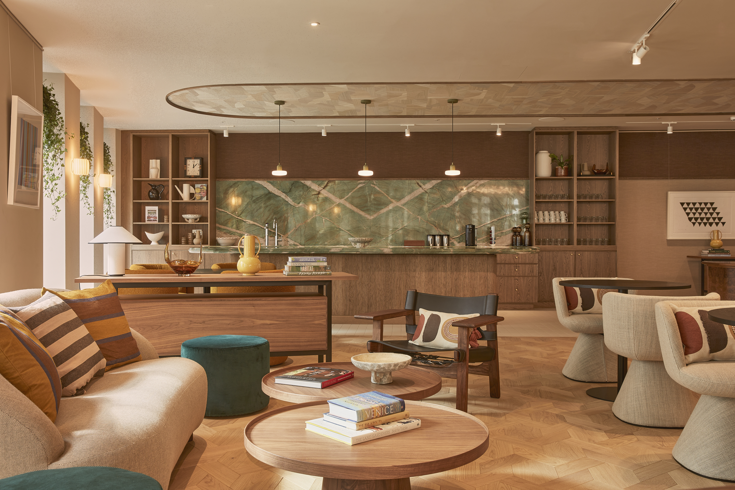 A contemporary lounge and kitchen area featuring comfortable seating, wooden coffee tables, a communal kitchen, open shelving and warm interior finishes.