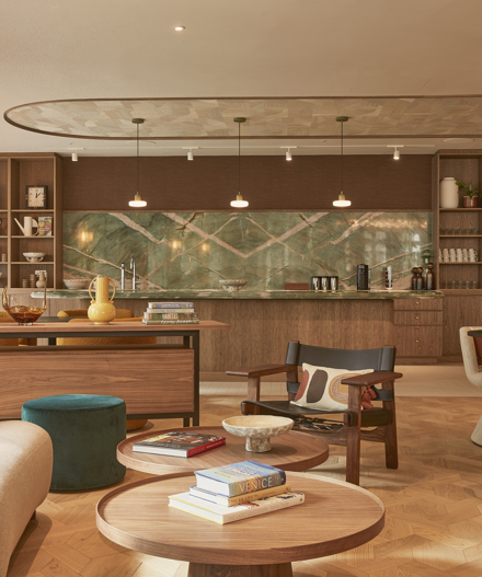 A contemporary lounge and kitchen area featuring comfortable seating, wooden coffee tables, a communal kitchen, open shelving and warm interior finishes.