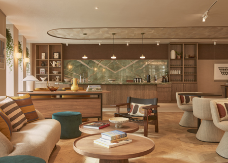 A contemporary lounge and kitchen area featuring comfortable seating, wooden coffee tables, a communal kitchen, open shelving and warm interior finishes.