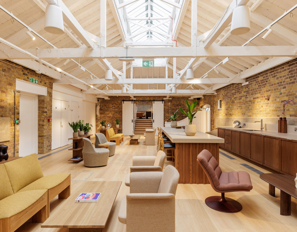 A contemporary lounge and communal kitchen featuring comfortable seating, a large kitchen island, exposed brick walls and a vaulted ceiling with skylights.