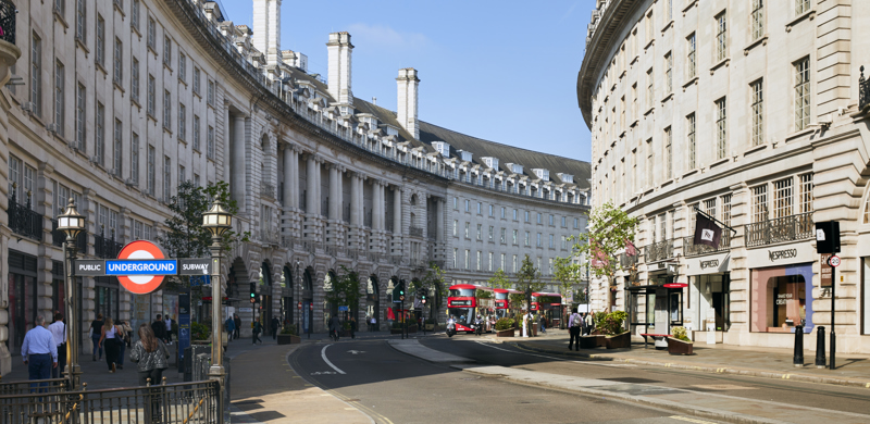 View of Regent Street in London featuring the Underground entrance, historic curved buildings, shops and a red double-decker bus on a sunny day.