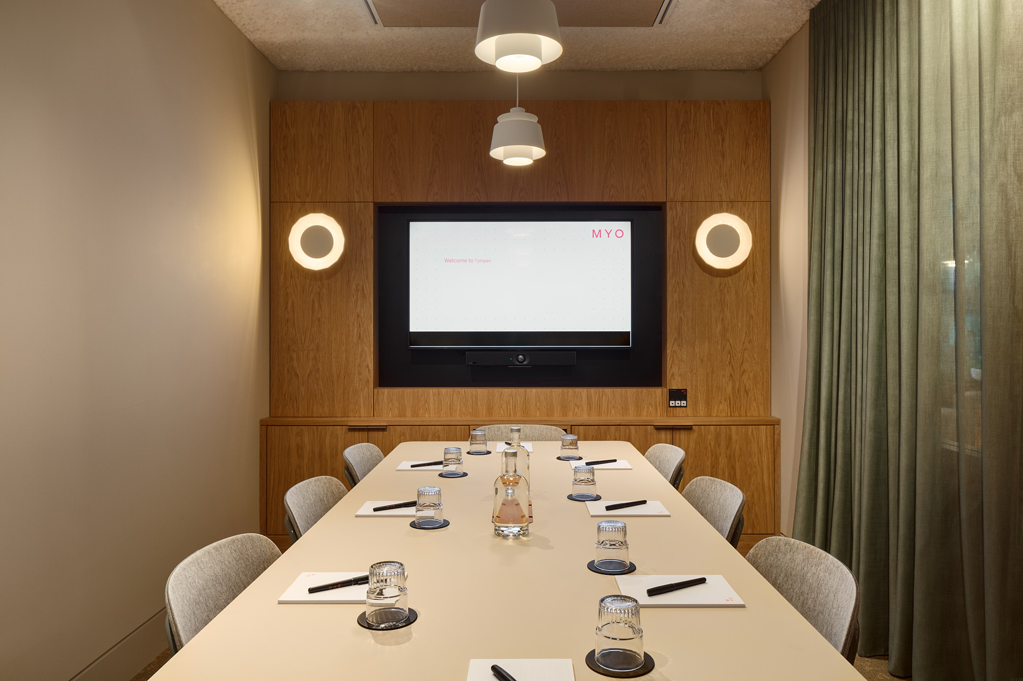 A contemporary boardroom featuring a conference table, upholstered chairs, a presentation screen, pendant lighting and timber wall panelling.