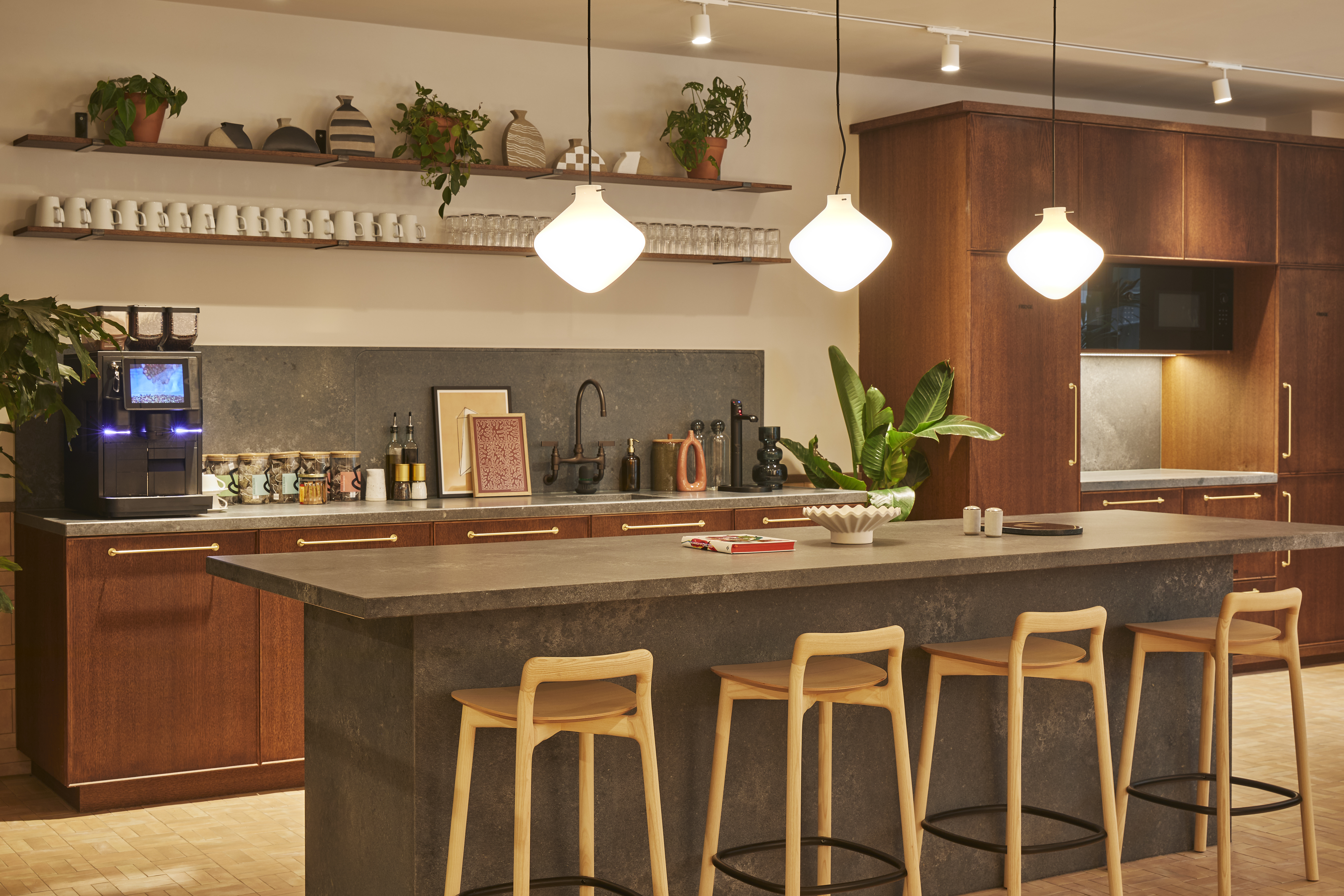 A contemporary communal kitchen featuring a large island with bar stools, coffee station, open shelving, pendant lighting and modern cabinetry.