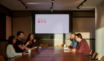Team meeting taking place in a contemporary boardroom at MYO Liverpool Street, featuring a large walnut conference table, integrated presentation screen and warm, ambient lighting.