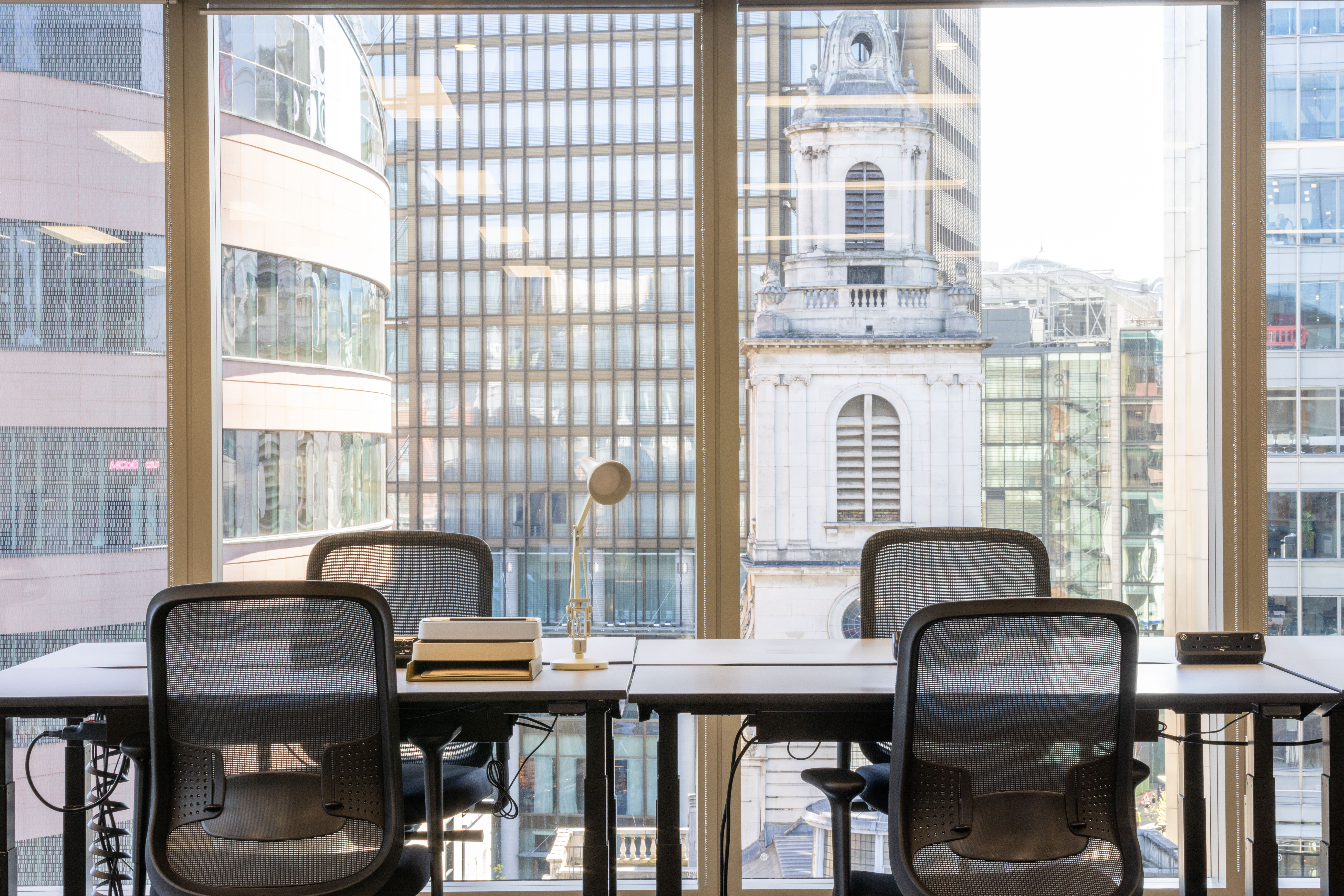 Dedicated workstations at MYO Liverpool Street with floor-to-ceiling windows overlooking the surrounding city skyline and historic architecture.