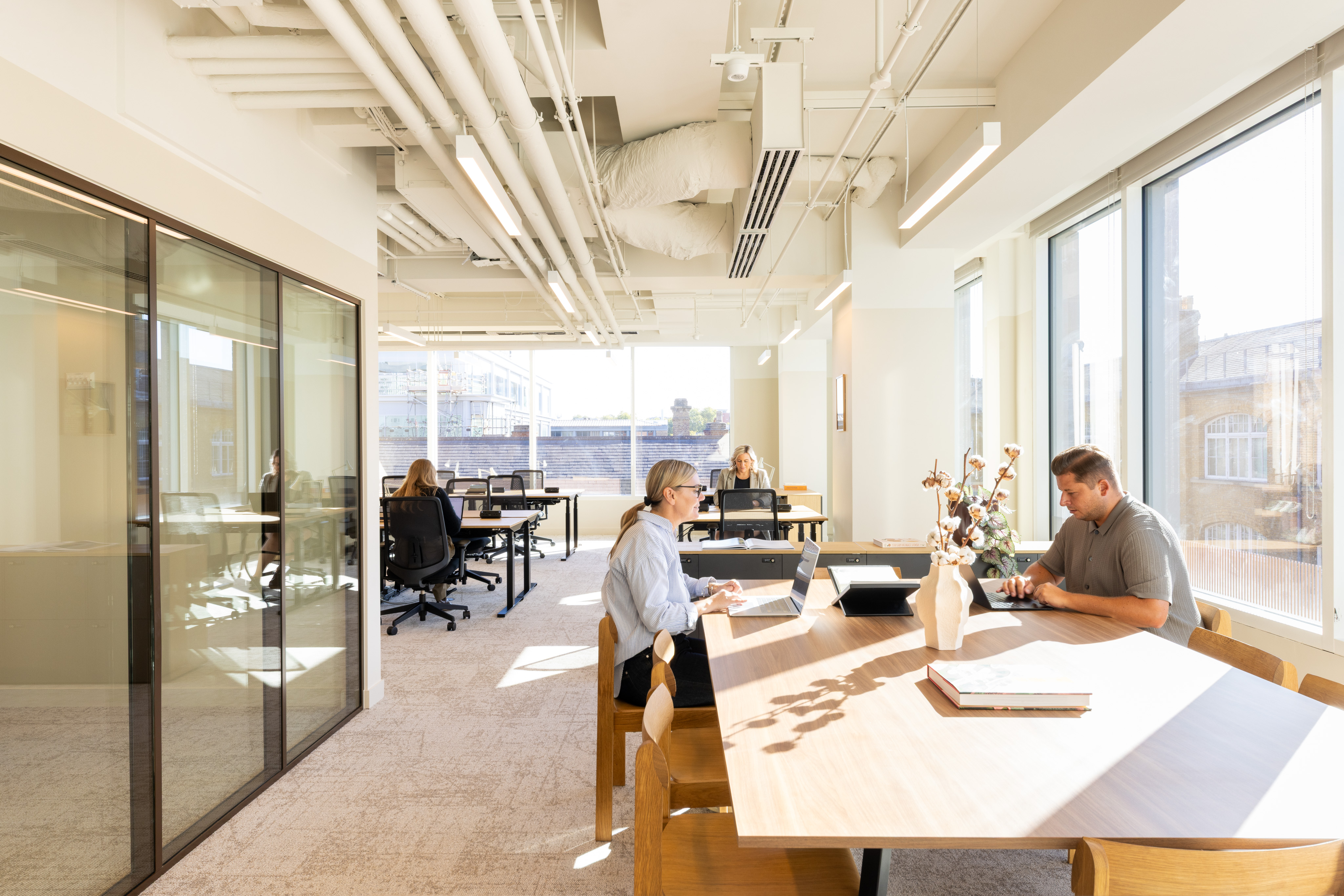 Professionals working in a bright open-plan workspace at MYO King's Cross, featuring communal desks, private meeting rooms and natural light.