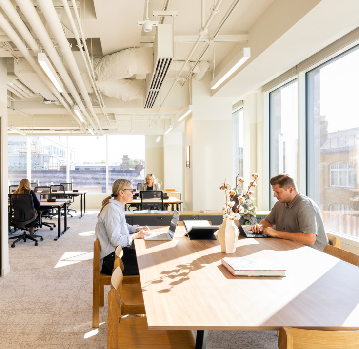 Professionals working in a bright open-plan workspace at MYO King's Cross, featuring communal desks, private meeting rooms and natural light.