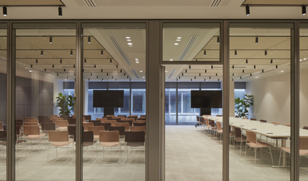 View through glass doors into a meeting space with rows of chairs, boardroom tables, large screens and floor-to-ceiling windows.