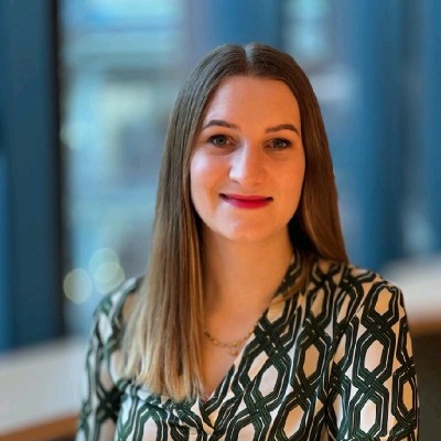 Portrait of a female MYO team member wearing a patterned blouse, photographed against a softly blurred backdrop of the workspace.