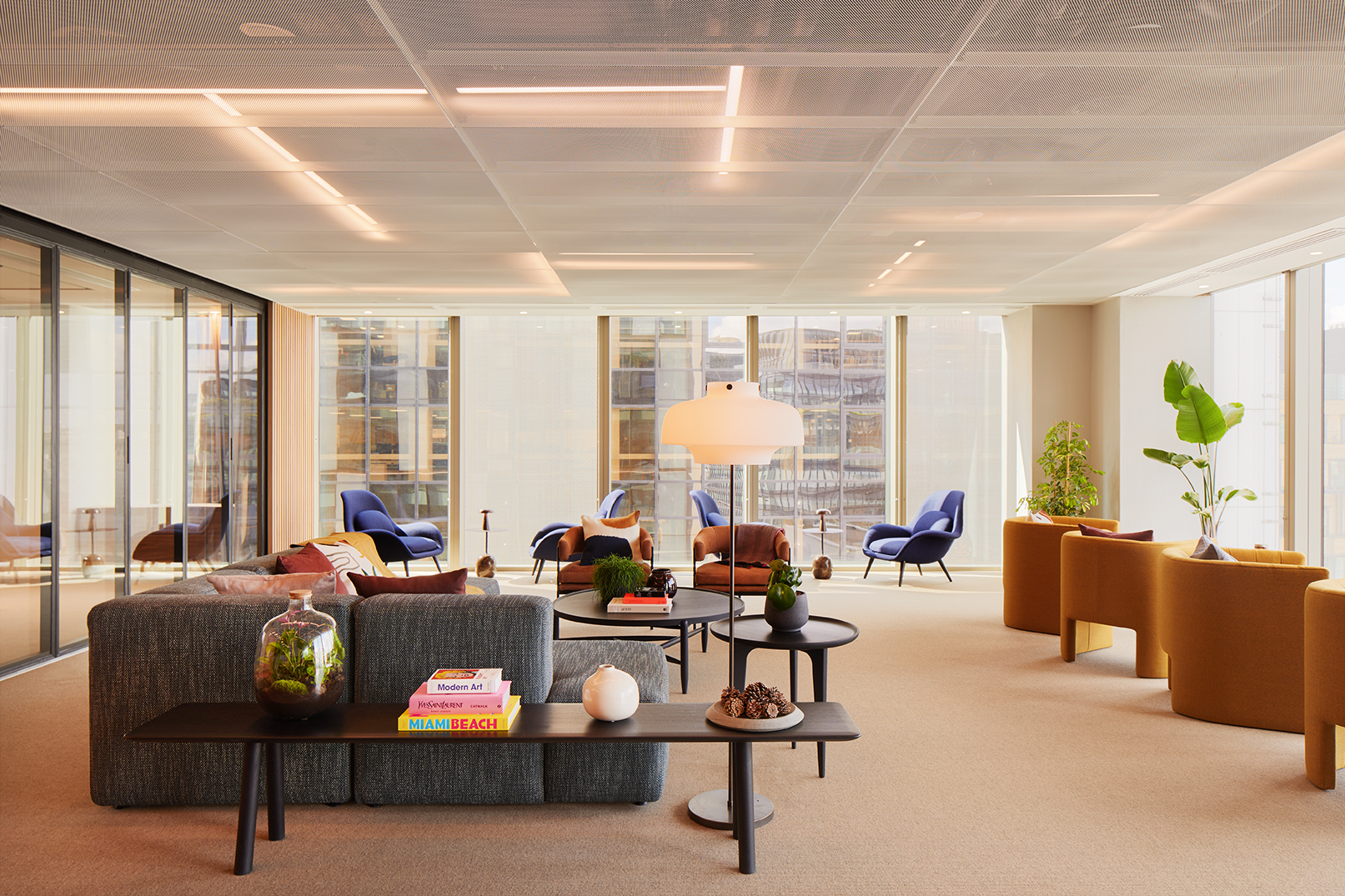 Lounge area at MYO Liverpool Street featuring soft textured sofas, burnt orange and navy armchairs, curated coffee table styling and floor-to-ceiling windows overlooking the city.