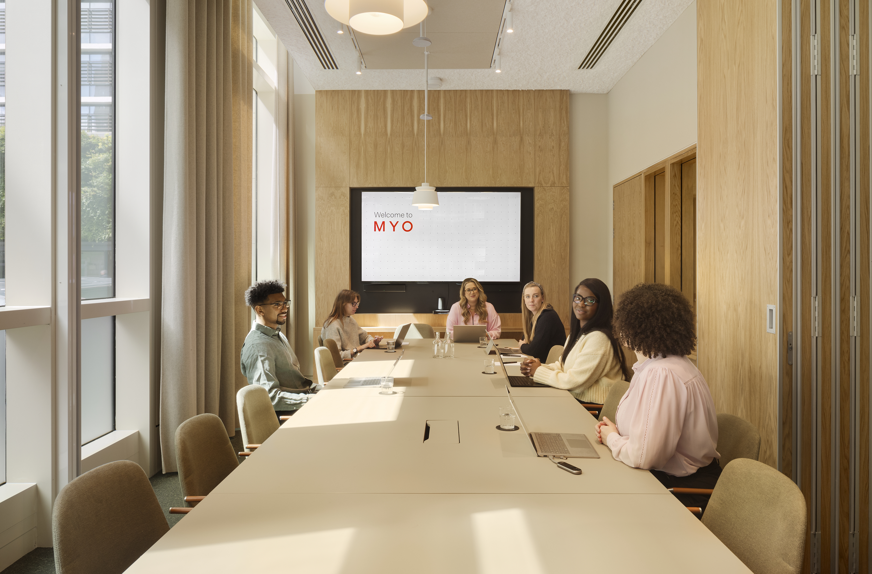 Meeting room at MYO New Street Square featuring a large conference table, upholstered seating, integrated presentation screen and a team gathered for a collaborative session.