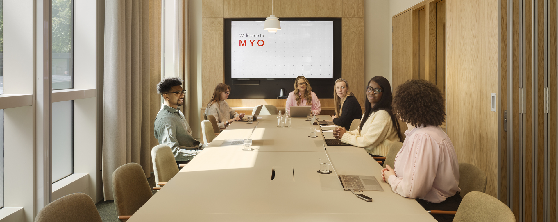 Meeting room at MYO New Street Square featuring a large conference table, upholstered seating, integrated presentation screen and a team gathered for a collaborative session.