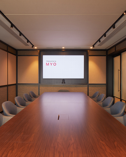 Boardroom at MYO Liverpool Street featuring a large walnut conference table, soft grey upholstered chairs, integrated presentation screen and warm ambient lighting.