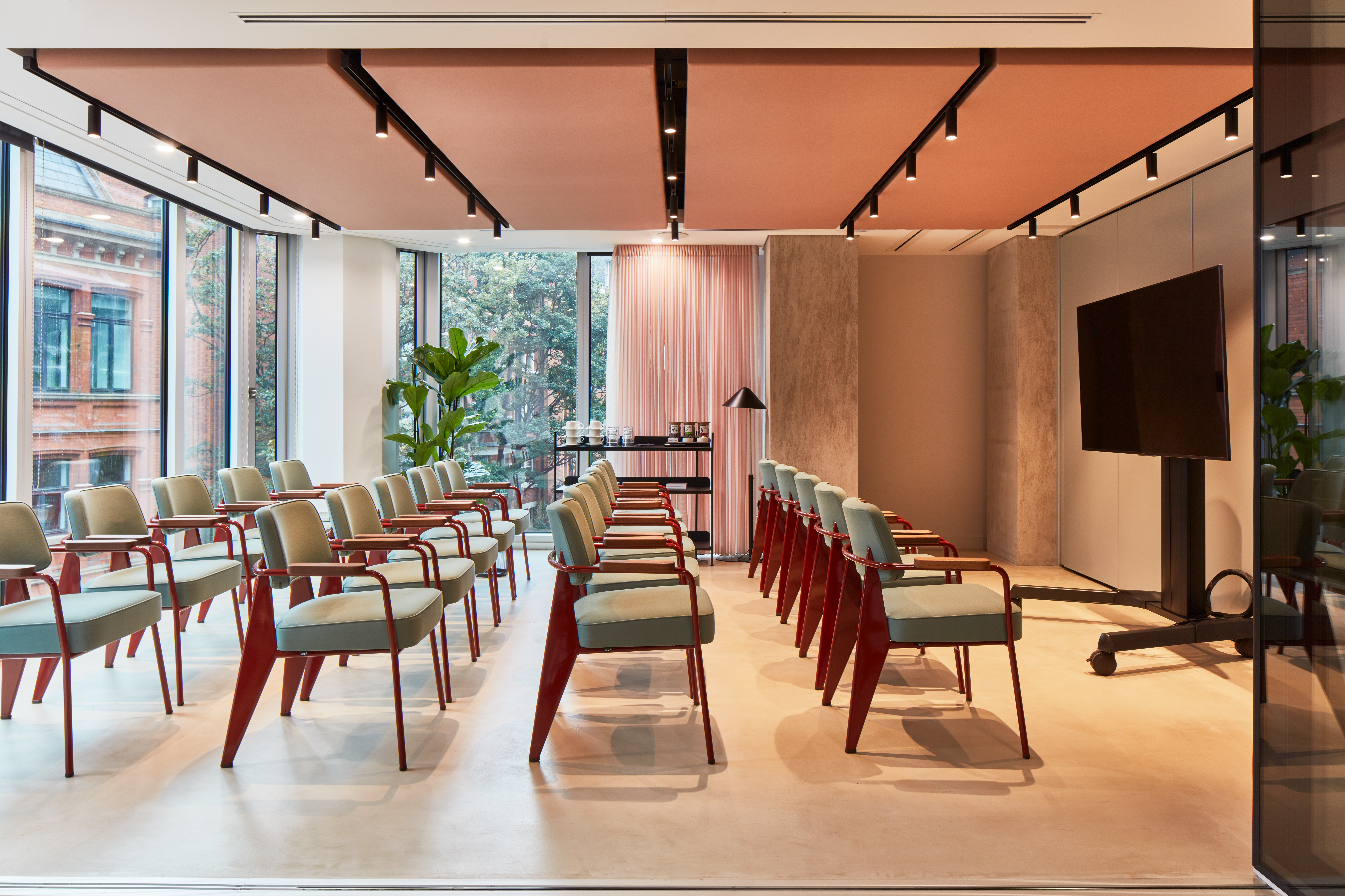 A contemporary event space with rows of chairs, a large presentation screen, floor-to-ceiling windows and modern lighting in a premium workspace.