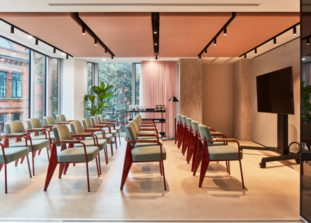 A contemporary event space with rows of chairs, a large presentation screen, floor-to-ceiling windows and modern lighting in a premium workspace.